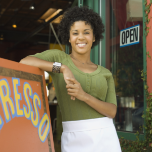 woman standing in front of coffee shop with open sign hanging from door